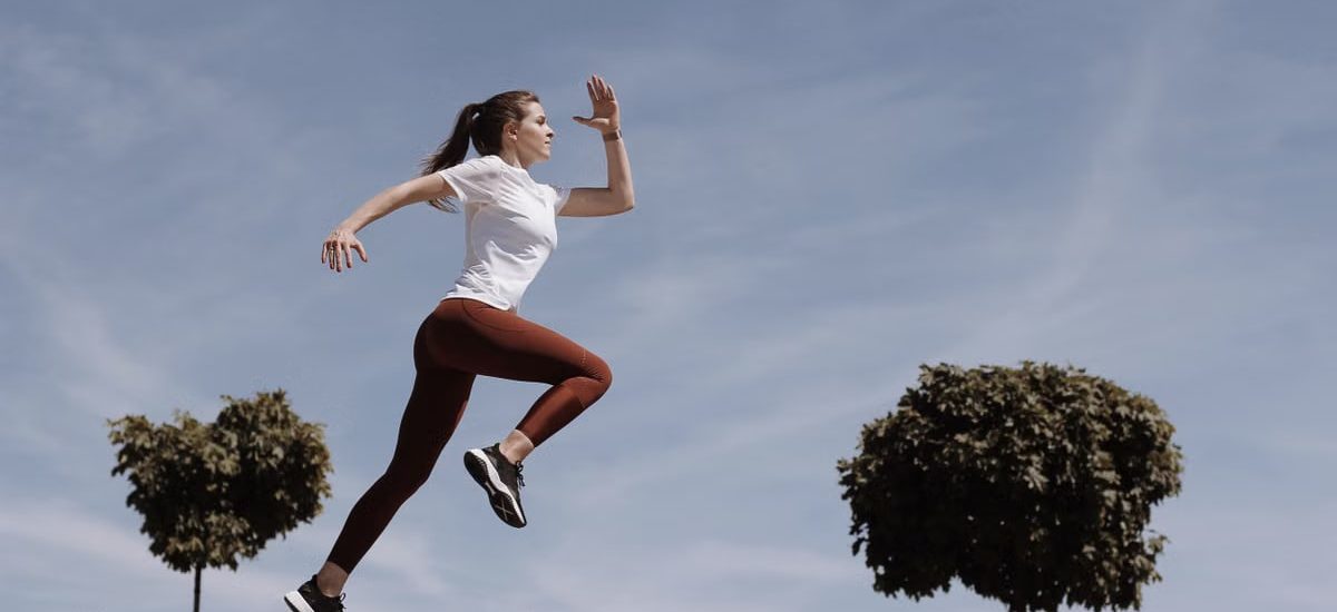 Athletic woman running on an outdoor road, demonstrating fitness and determination under a blue sky.