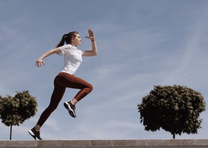 Athletic woman running on an outdoor road, demonstrating fitness and determination under a blue sky.